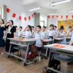 Children and teachers saluting in a colorful classroom decorated with flags.