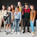 Group of diverse teenagers posing with their teacher in a modern classroom.
