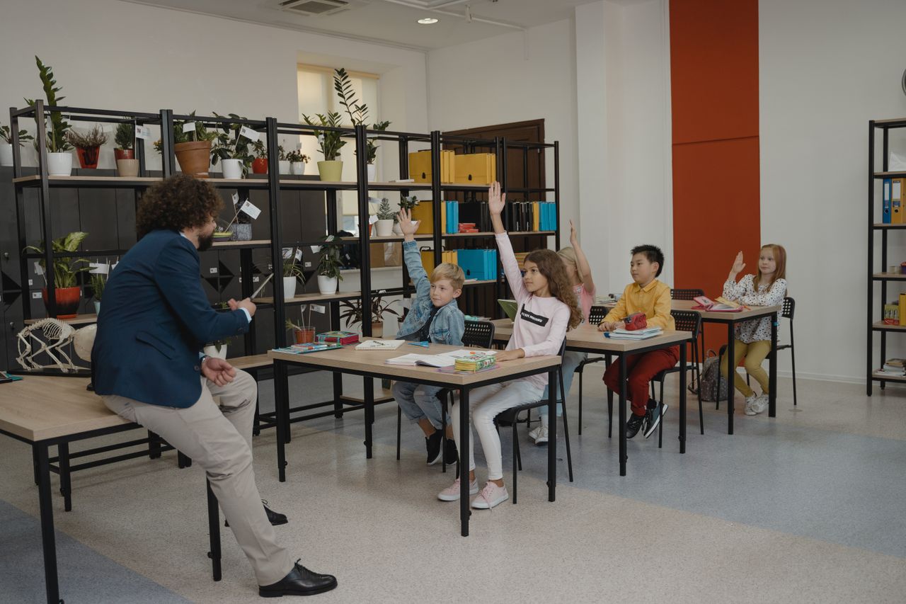 Students actively participating by raising hands in a modern classroom with attentive teacher and organized environment.