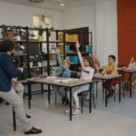 Students actively participating by raising hands in a modern classroom with attentive teacher and organized environment.