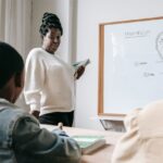 African American female teacher standing near whiteboard and explaining scheme to pupils during lesson in school